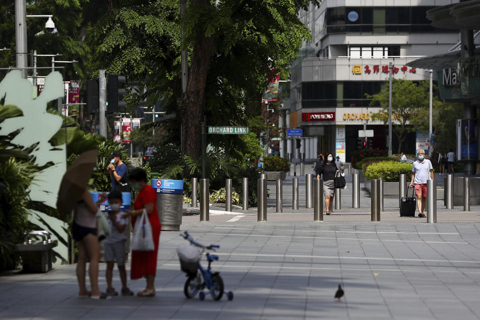 People wearing protective face masks walk along the Orchard Road shopping belt in Singapore, Friday, April 10, 2020. The Singapore government put in place "circuit breaker" measures in the light of a sharp increase of COVID-19 cases in recent days. Under the measures which will last through May 4, people have to stay home and step out only for essential tasks, such as going to work if they are in essential services, buying food and groceries, or for a short bout of exercise. (AP Photo/Yong Teck Lim)