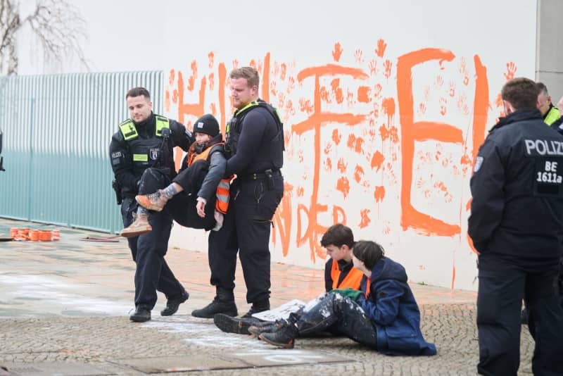 A Last Generation climate activist is carried away by police officers while "Help! Your children" is written in orange on the Chancellery wall. Annette Riedl/dpa