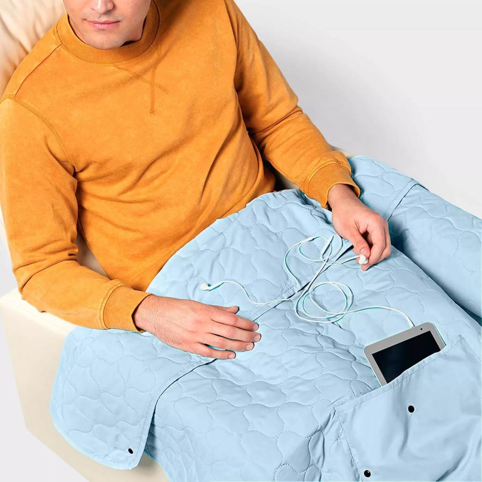 Person sitting with the light blue blanket covering their legs, with a tablet tucked into a pocket