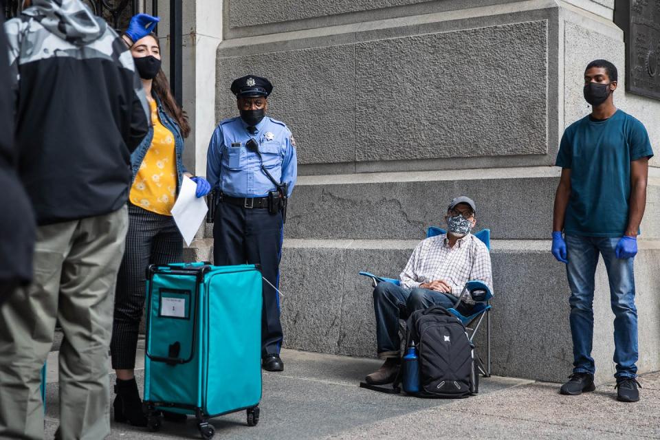 Man sits in folding chair near a line of voters and a police officer