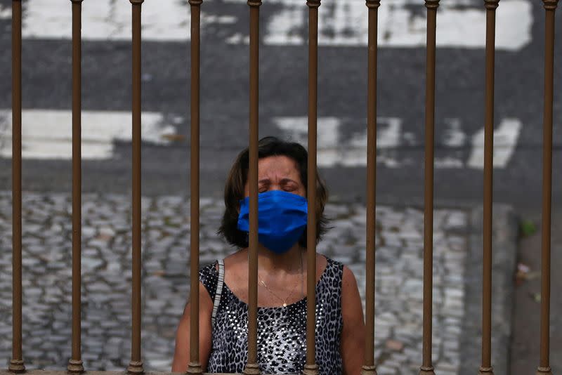 A woman wearing a protective face mask prays outside a church as priest Jorge Luiz de Oliveira delivers the Angelus prayer from the balcony of the Santuario Basilica de Sao Sebastiao, following the coronavirus disease (COVID-19) outbreak, in Rio de Janeiro