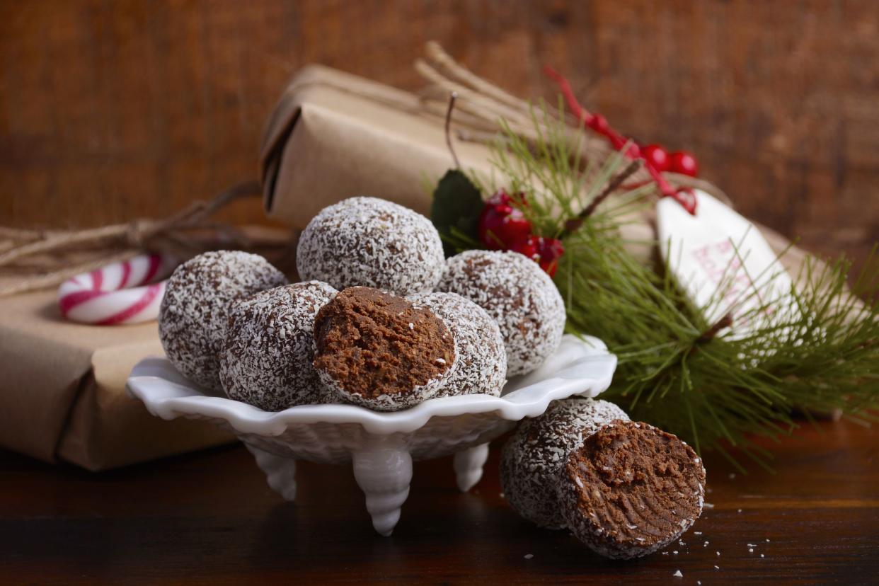 Traditional Christmas Rum Ball candy spotlighted in festive setting with rustic style gifts and decorations on dark vintage wood background, closeup.