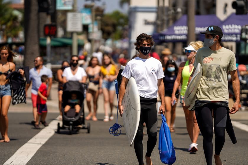 HUNTINGTON BEACH, CA - SEPTEMBER 04: Surfers wearing face coverings cross the street towards the Huntington Beach Pier, on Friday, Sept. 4, 2020 in Huntington Beach, CA. As California braces for a looming heatwave Gov. Gavin Newsom issued an emergency proclamation aimed at shoring up the state's energy capacity with scorching temperatures being set to sear the state through the Labor Day weekend. (Kent Nishimura / Los Angeles Times)