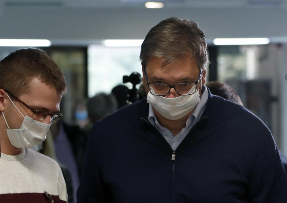 Serbia's President Aleksandar Vucic, right, wearing a face mask to protect against coronavirus, arrives at a polling station in Belgrade, Serbia, Sunday, June 21, 2020. Serbia's ruling populists are set to tighten their hold on power in a Sunday parliamentary election held amid concerns over the spread of the coronavirus in the Balkan country and a partial boycott by the opposition. (AP Photo/Darko Vojinovic)