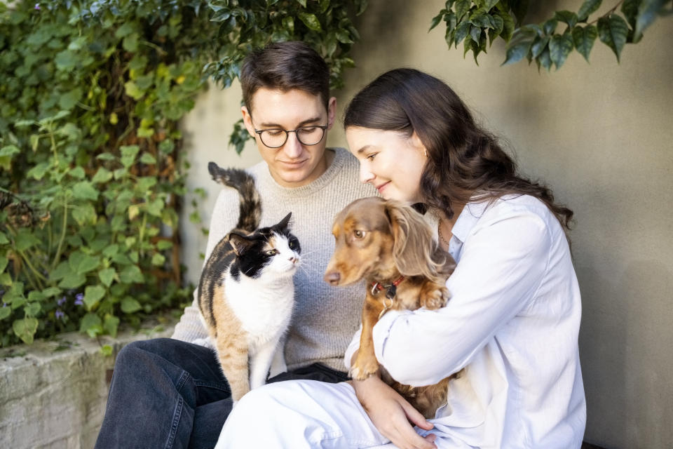 Young man and woman sitting in backyard holding a cat and a dog