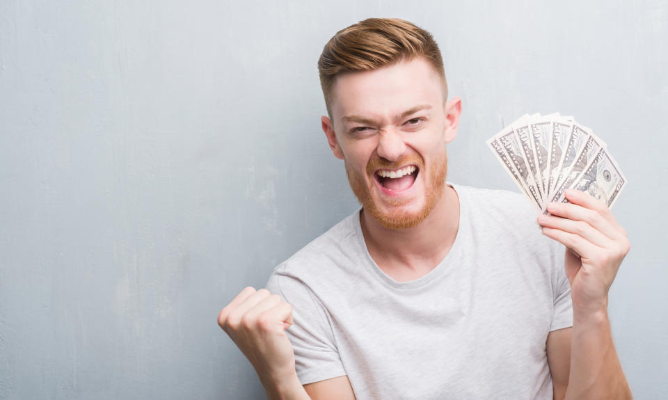 Man against gray background smiling and holding a bunch of 50-dollar bills