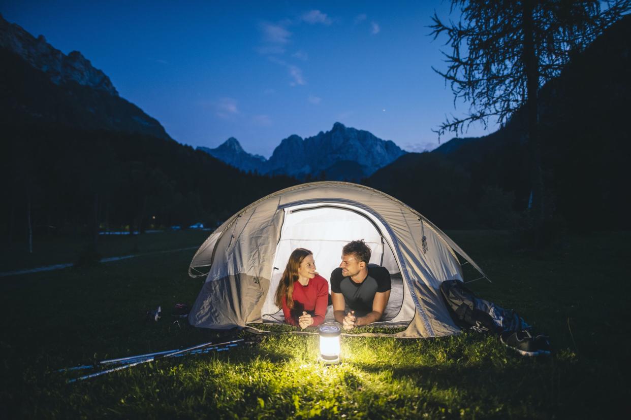 Relaxed couple in 20s and 30s lying on tent porch and smiling as they admire twilight view of scenic beauty in northwestern Slovenia.