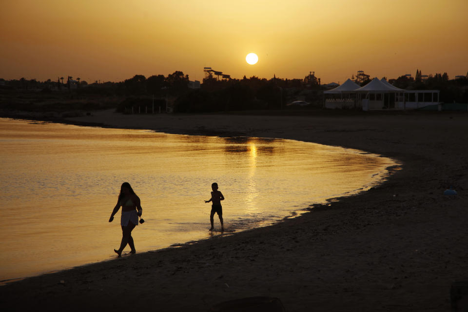 Beachgoers walks at the sea water during sunset at an empty stretch of Dome beach hotel at Makrinissos in Cyprus' seaside resort of Ayia Napa, a favorite among tourists from Europe and beyond, on Sunday, May 17, 2020. With coronavirus restrictions gradually lifting, Cyprus authorities are mulling ways to get holidaymakers back to the tourism-reliant island nation. (AP Photo/Petros Karadjias)