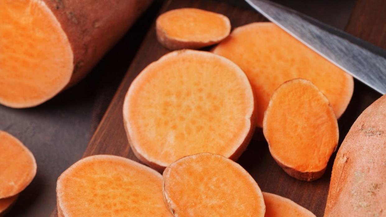 fresh sweet potatoes whole and sliced on wooden kitchen board from above