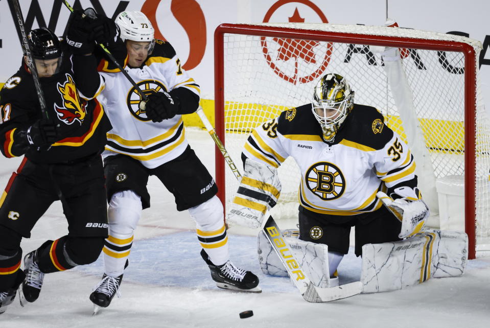 Boston Bruins defenseman Charlie McAvoy, center, keeps Calgary Flames forward Mikael Backlund, left, away from the puck as goalie Linus Ullmark watches during the second period of an NHL hockey game Tuesday, Feb. 28, 2023, in Calgary, Alberta. (Jeff McIntosh/The Canadian Press via AP)