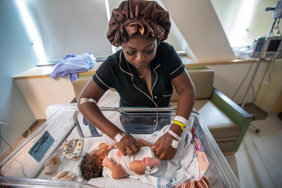 A woman attends to a baby in a hospital bassinet.