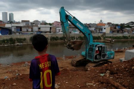 A child watches as an excavator cleans the Ciliwung river bank at Jatinegara district in Jakarta, Indonesia, December 29, 2016. Picture taken December 29, 2016. REUTERS/Beawiharta