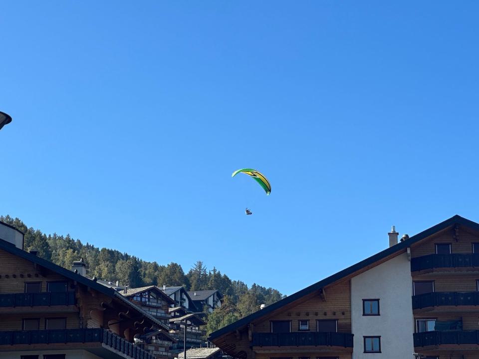 paraglider under a green yellow parachute above swiss cabin-style hotels