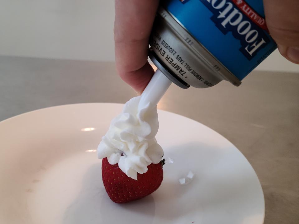hand spraying foodtown whipped cream on to a strawberry