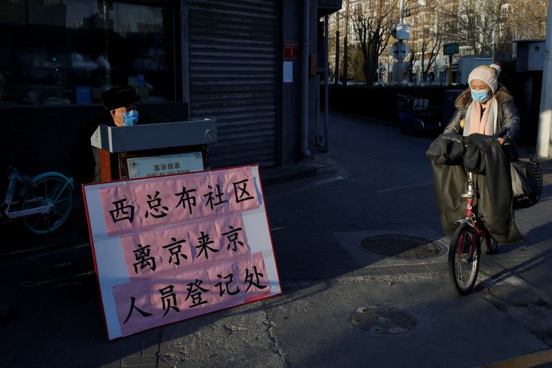 A woman wearing a face mask rides her bicycle in front of a registration point for people leaving or returning to Beijing, as the country is hit by an outbreak of the new coronavirus, in Beijing