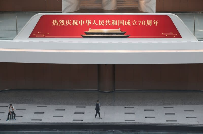 People are seen next to a sign celebrating the 70th founding anniversary of the People's Republic of China at the terminal hall of the newly launched Daxing International Airport on the outskirts Beijing