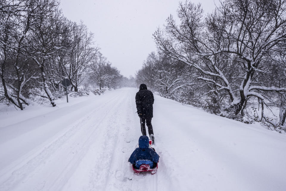 A man pulls a child on a sleigh, during a heavy snowfall in Bustarviejo, outskirts of Madrid, Spain, Saturday, Jan. 9, 2021. A persistent blizzard has blanketed large parts of Spain with 50-year record levels of snow, halting traffic and leaving thousands trapped in cars or in train stations and airports that suspended all services as the snow kept falling on Saturday. Half of Spain is on alert, with five provinces on their highest level of warning. (AP Photo/Bernat Armangue)