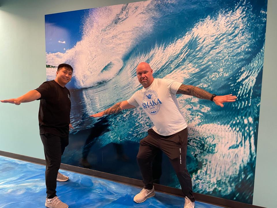 Thinh Tran (left) and Casey Felkins pretend to surf a wave in front of a "selfie" wall at Shaka Café in Howell on Tuesday, Oct. 10, 2023.