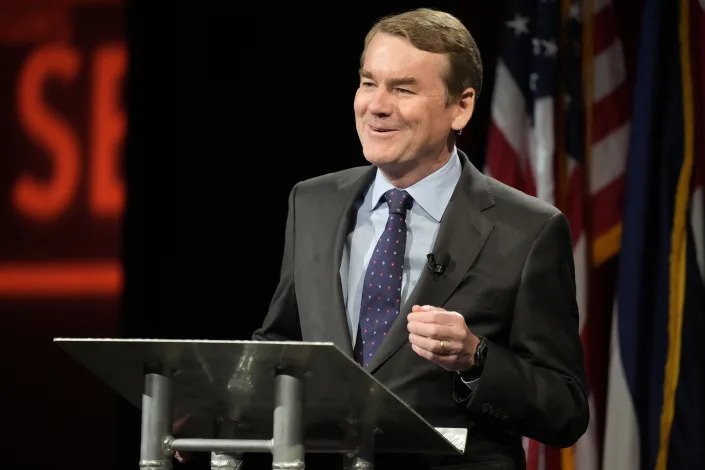 Sen. Michael Bennet at the podium, looking amused.