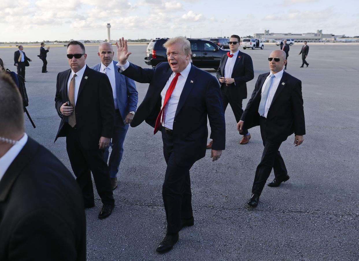 Then-President Donald Trump, center, surrounded by members of the Secret Service, walks across the tarmac to begin to greet supporters during his arrival at Palm Beach International Airport, in West Palm Beach, Fla., April 18, 2019. 