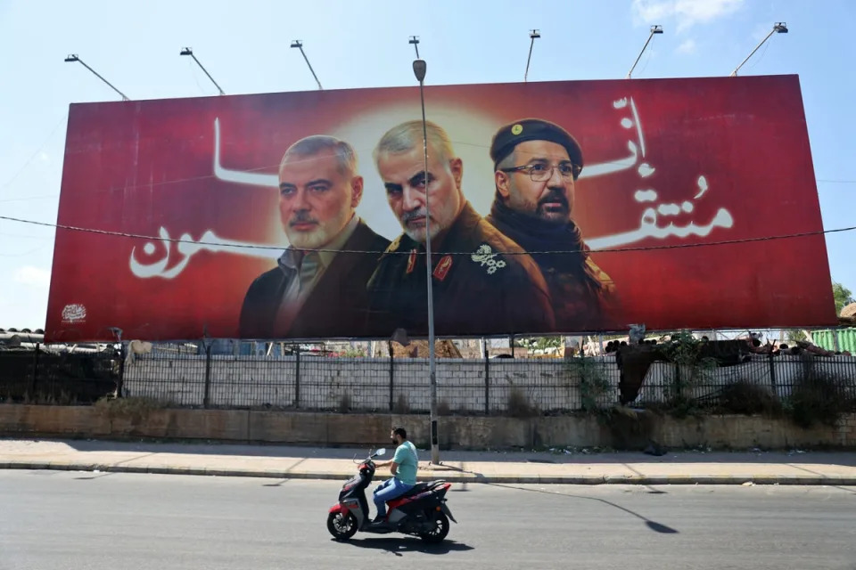 A man rides his moped past a billboard near Beirut International Airport bearing portraits of Hamas leader Ismail Haniyeh, Hezbollah commander Fuad Shukr and Iranian Quds Force chief Qassem Soleimani (AFP via Getty Images)