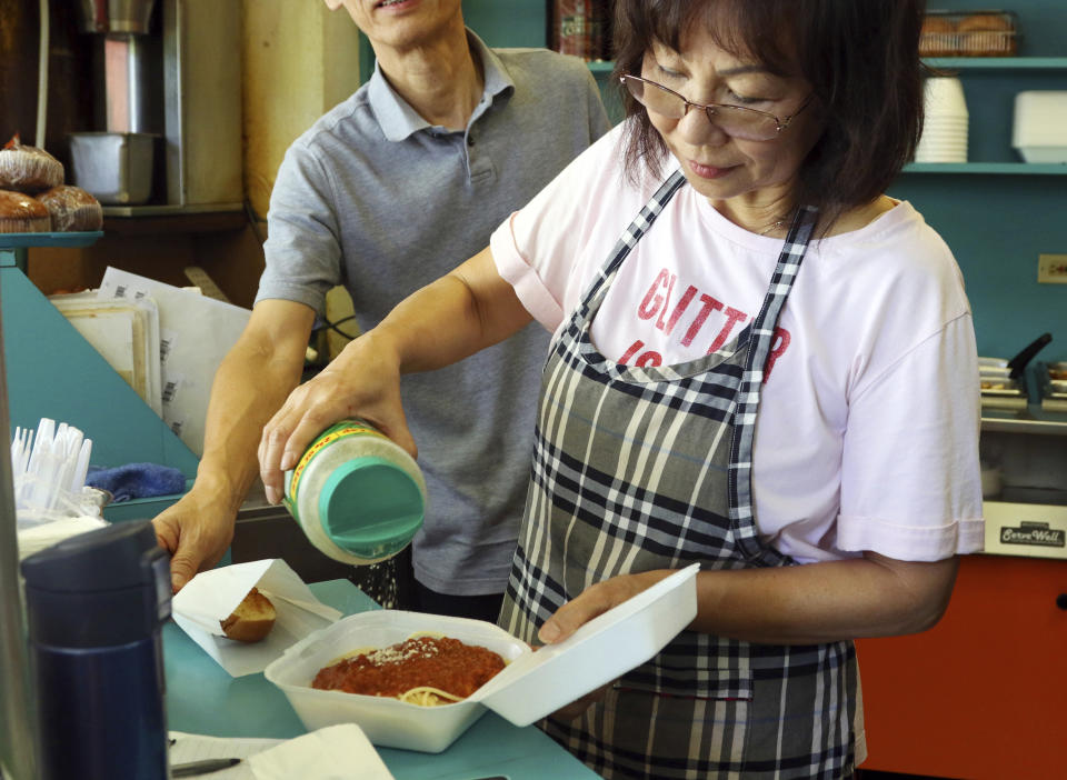 In this Thursday, March 14, 2019 photo, Belinda Lau, manager of the Wiki Wiki Drive Inn takeout restaurant in Honolulu, sprinkles cheese on an order of spaghetti in a styrofoam container. Hawaii would be the first state in the U.S. to ban most plastics used at restaurants under legislation that aims to cut down on waste that pollutes the ocean. Dozens of cities across the country have banned plastic foam containers, but Hawaii would be the first to bar them statewide. (AP Photo/Audrey McAvoy)