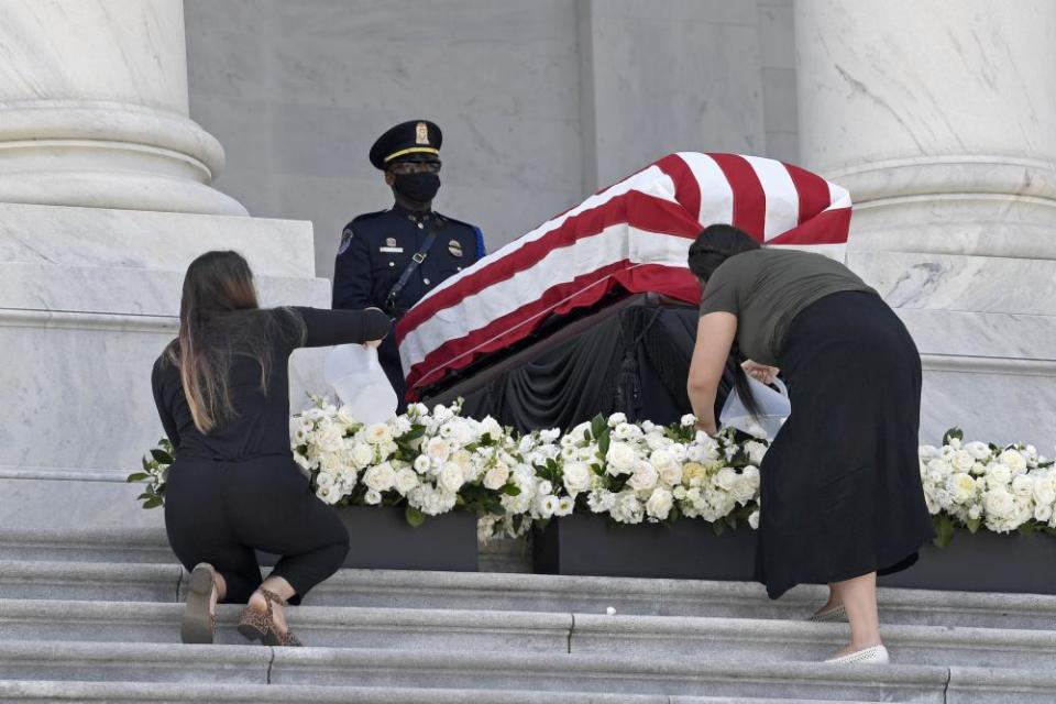 Two women water the flowers near the flag-draped casket on Tuesday.