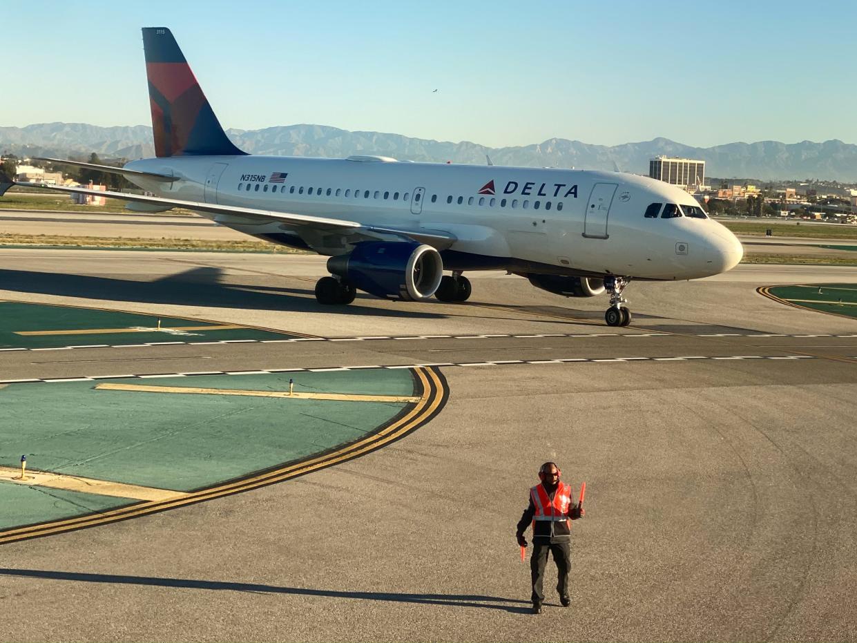 FILE PHOTO: An airport worker guides a Delta Air Lines Airbus A319-100 plane on the tarmac at LAX in Los Angeles, California, U.S., January 6, 2020. REUTERS/Lucy Nicholson