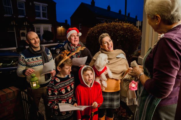 Three generation family are doing door-to-door carol singing. There is a senior woman at the door, appreciating their singing.