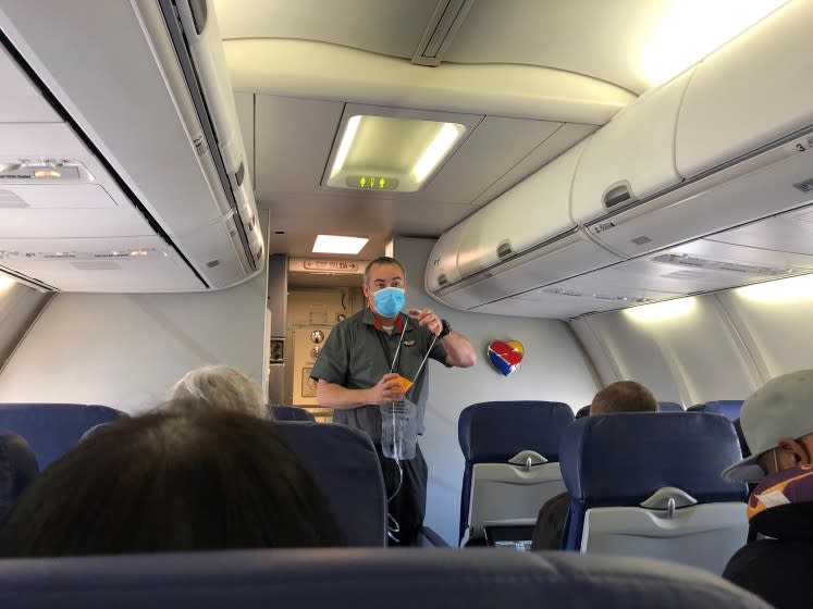 Flight attendant, wearing one mask, demonstrates the use of another at the outset of a Burbank-Las Vegas flight in early June.