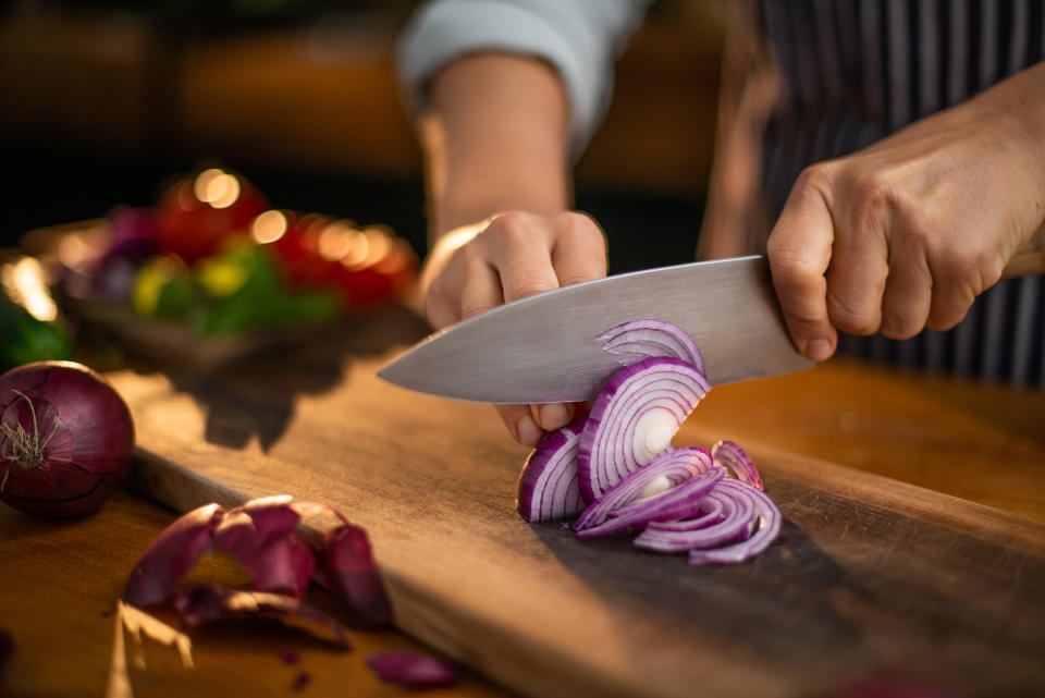 A cook cuts red onions on a wooden cutting board. (Getty)