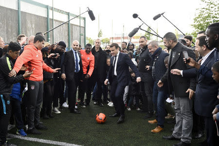 Emmanuel Macron (C), head of the political movement En Marche !, or Onwards !, and candidate for the 2017 presidential election, kicks a soccer ball during a campaign visit in Sarcelles, near Paris, April 27, 2017. REUTERS/Martin Bureau/Pool