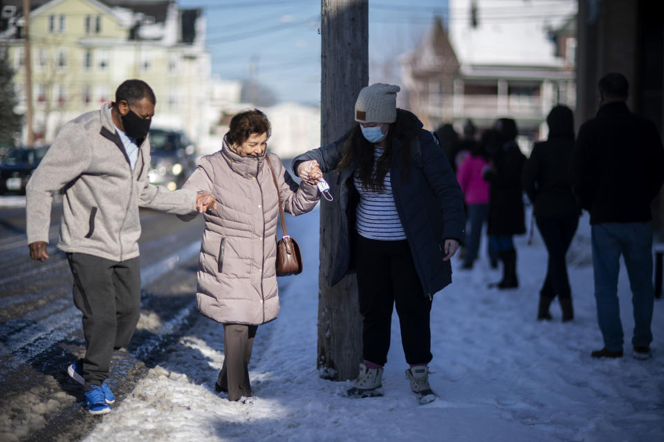 Maria Manazaz, center, is helped by Manny Riposa, left, and a fellow resident to get in line for her vaccine at a clinic in Central Falls, R.I., Saturday Feb. 20, 2021. Nearly a third of adults in the city have received at least one dose of vaccine, according to state data. Health officials say the city of about 20,000 has seen a marked drop in COVID-19 cases as a result. (AP Photo/David Goldman)