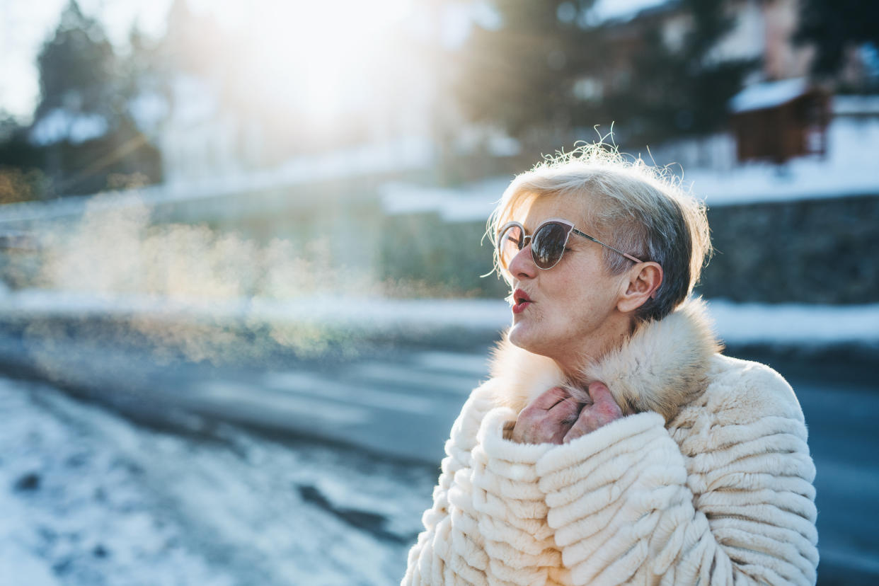 A confident female pensioner with sunglasses on a walk in town in cold weather.