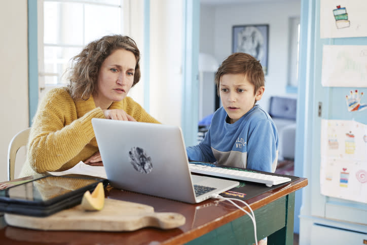 Mother homeschooling son at laptop.