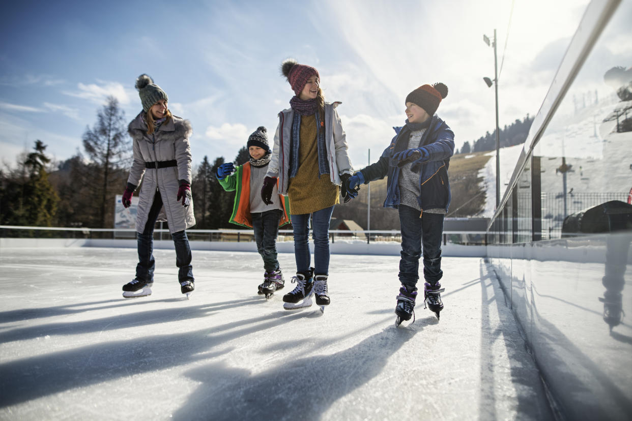 Mother and three kids spending time on ice-skating rink. 