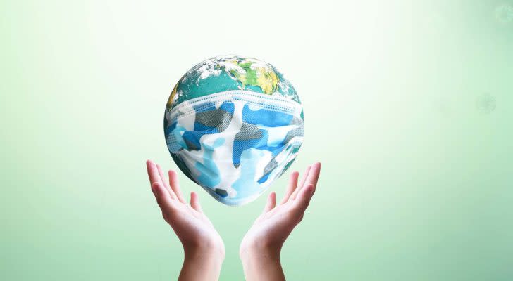 A digital image of hands holding up the planet Earth, which is wearing a face mask.