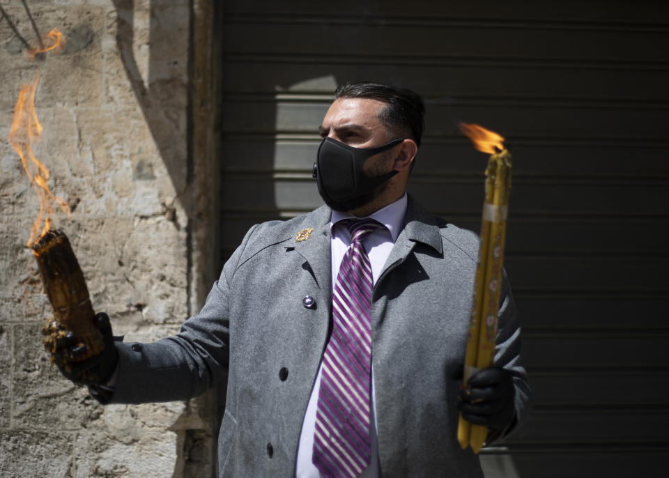 Issa Kassissieh wears a mask and gloves as he holds candles lit from holy fire from the Church of the Holy Sepulchre, traditionally believed by many Christians to be the site of the crucifixion and burial of Jesus Christ, in Jerusalem's old city after the traditional Holy Fire ceremony was called off amid coronavirus, Saturday, April 18, 2020. A few clergymen on Saturday marked the Holy Fire ceremony as the coronavirus pandemic prevented thousands of Orthodox Christians from participating in one of their most ancient and mysterious rituals at the Jerusalem church marking the site of Jesus' tomb.(AP Photo/Ariel Schalit)