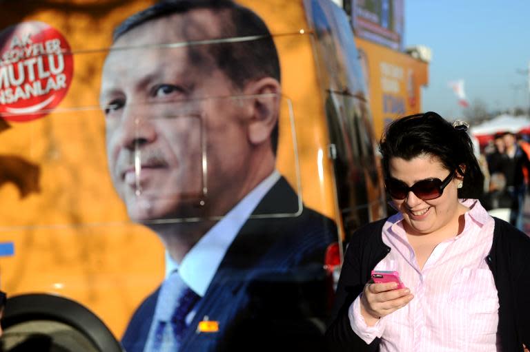 A Turkish woman looks at her smartphone as she walks by a banner displaying a portrait of Turkish prime minister Recep Tayyip Erdogan, in Istanbul, on March 21, 2014