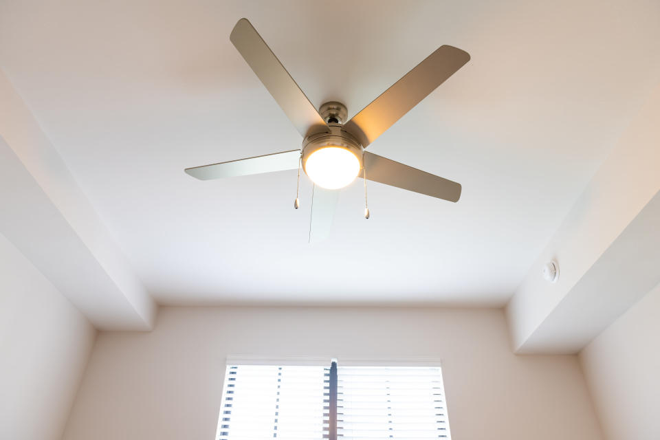 A ceiling fan with five blades and a central light fixture is mounted on the ceiling. A window with closed blinds is visible below the fan