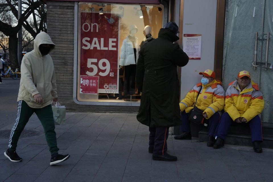 Workers rest outside a shop with a sale promotion sign in Beijing, Thursday, Dec. 29, 2022. China is on a bumpy road back to normal life as schools, shopping malls and restaurants fill up again following the abrupt end of some of the world's most severe restrictions even as hospitals are swamped with feverish, wheezing COVID-19 patients. (AP Photo/Ng Han Guan)