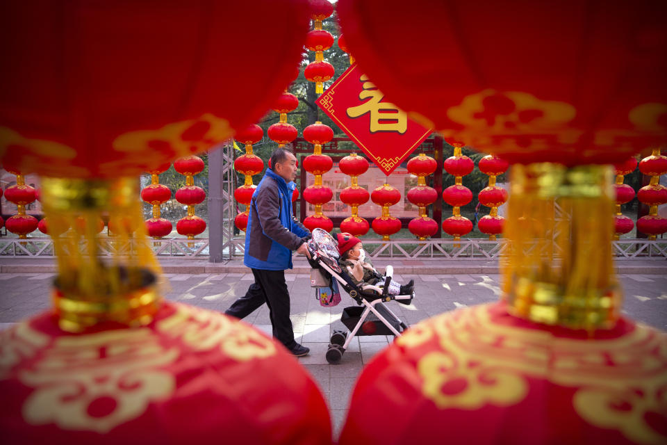 A man pushes a child in a stroller wearing a face mask past decorations for a canceled Lunar New Year temple fair at Longtan Park in Beijing, Saturday, Jan. 25, 2020. China's most festive holiday began in the shadow of a worrying new virus Saturday as the death toll surpassed 40, an unprecedented lockdown kept 36 million people from traveling and authorities canceled a host of Lunar New Year events. (AP Photo/Mark Schiefelbein)