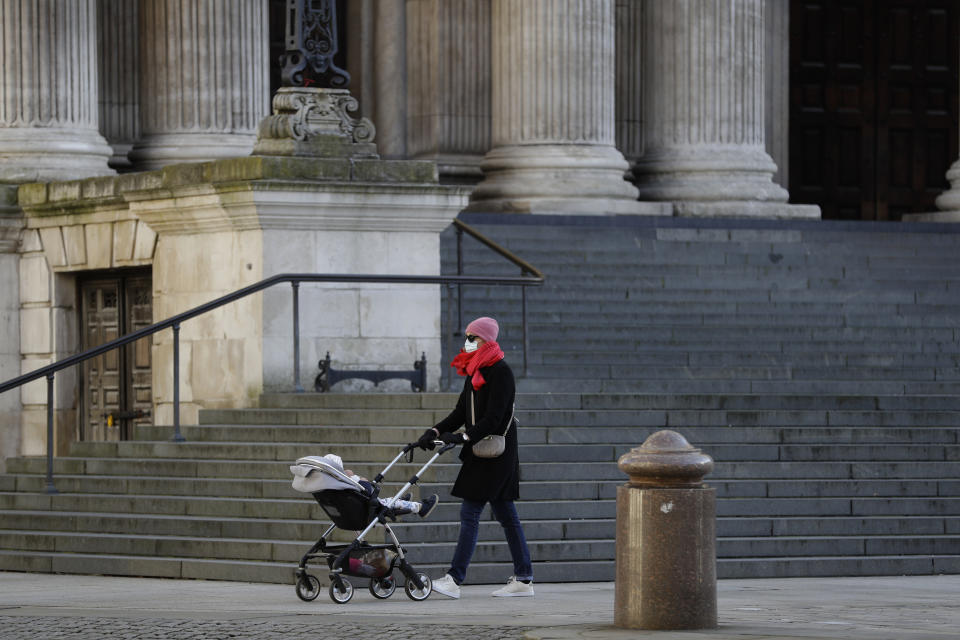 A woman wearing a face mask to curb the spread of coronavirus pushes a child in a buggy past the steps of St. Paul's Cathedral, in the City of London financial district of London, Friday, Jan. 22, 2021, during England's third national lockdown since the coronavirus outbreak began. The U.K. is under an indefinite national lockdown to curb the spread of the new variant, with nonessential shops, gyms and hairdressers closed, most people working from home and schools largely offering remote learning. (AP Photo/Matt Dunham)