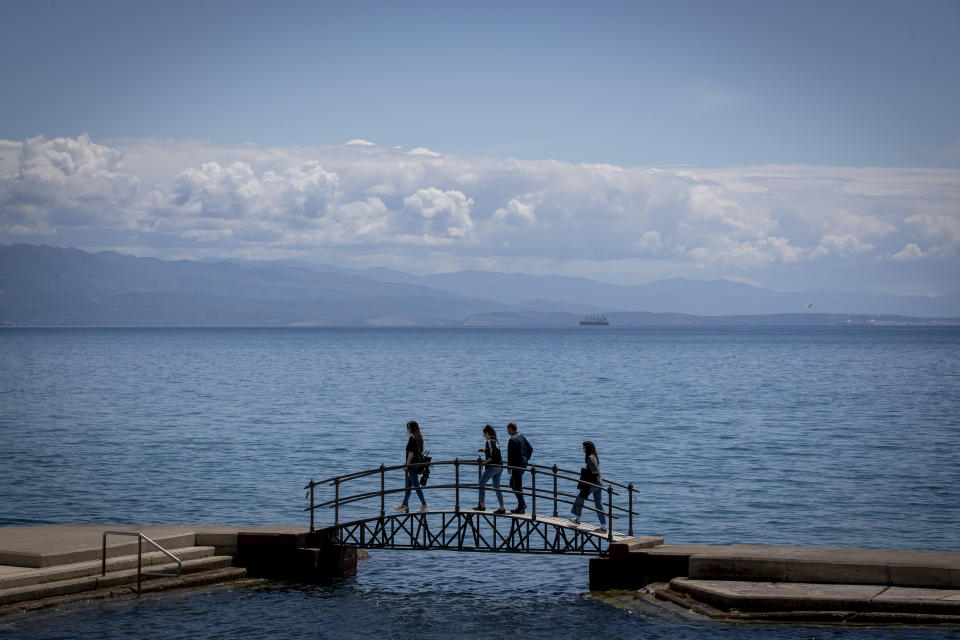 A group of tourists walk across a bridge on the seafront in Opatija, Croatia, Saturday, May 15, 2021. Croatia has opened its stunning Adriatic coastline for foreign tourists after a year of depressing coronavirus lockdowns and restrictions. (AP Photo/Darko Bandic)