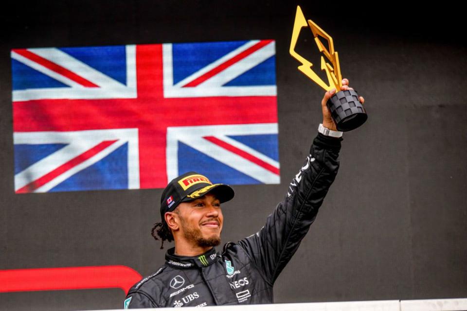 lewis hamilton holding up a trophy with his left hand in front of a british flag