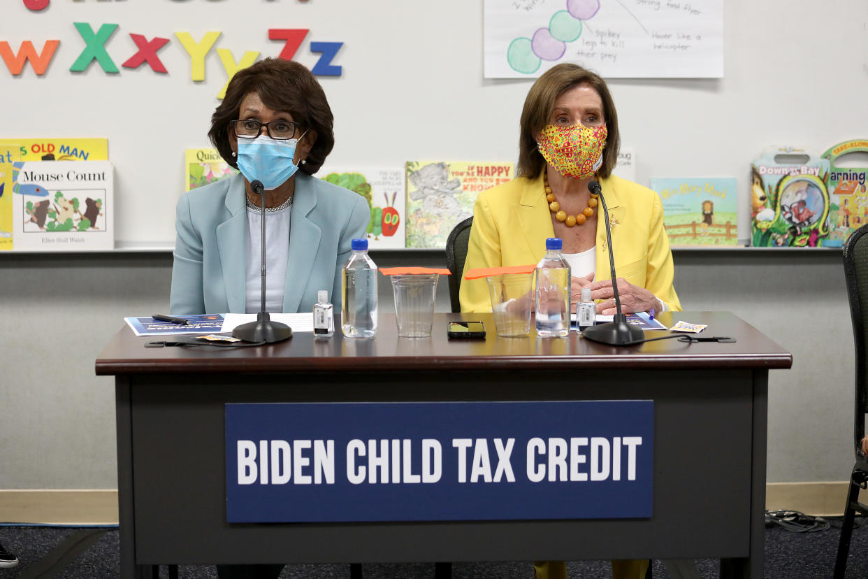 Rep. Maxine Waters and House Speaker Nancy Pelosi sit together at a desk with a 'Biden child tax credit' sign.