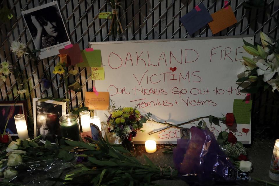 FILE - In this Monday, Dec. 5, 2016, file photo, candles, photos and flowers are placed at a makeshift memorial near the site of a massive warehouse fire in Oakland, Calif. Micah Allison, the wife of the founder of a ramshackle Oakland artists' colony where dozens of people burned to death in a fire last month says she's sorry about what happened but is angry about what she called "pretty terrible" treatment by the media and ex-neighbors. (AP Photo/Marcio Jose Sanchez, File)