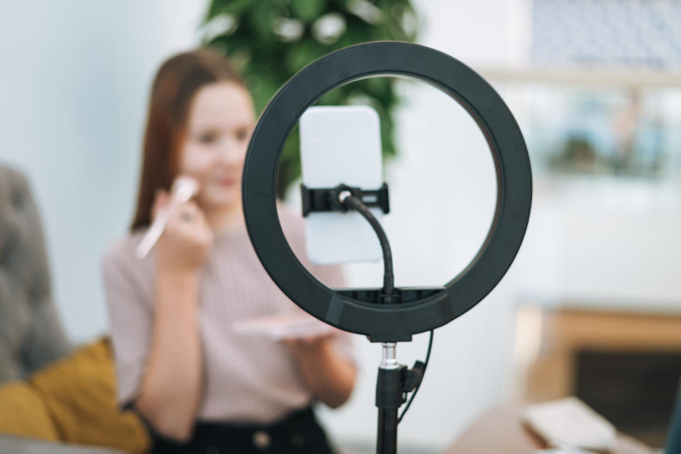 A woman applying makeup in front of her phone, which is positioned on a ring light