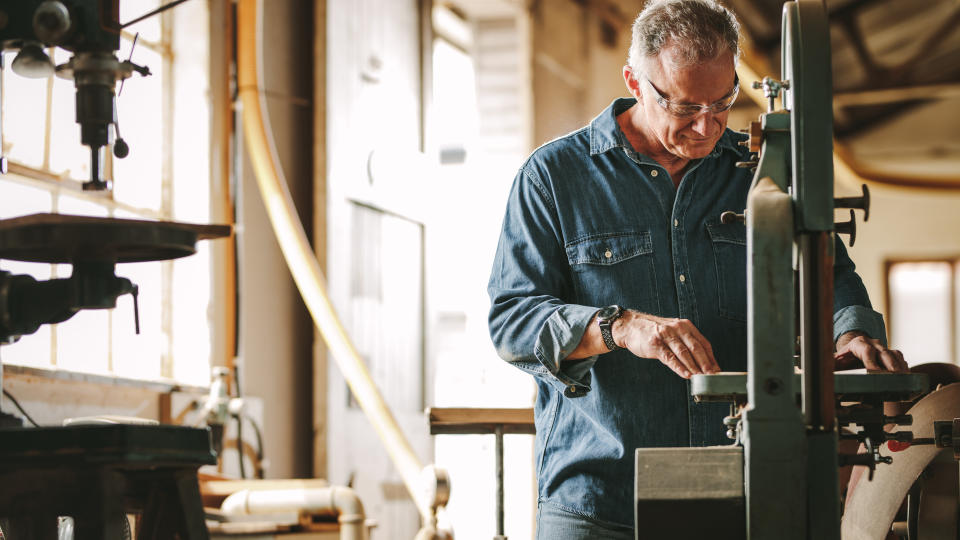 Mature male carpenter working on band saw machine in carpentry workshop.