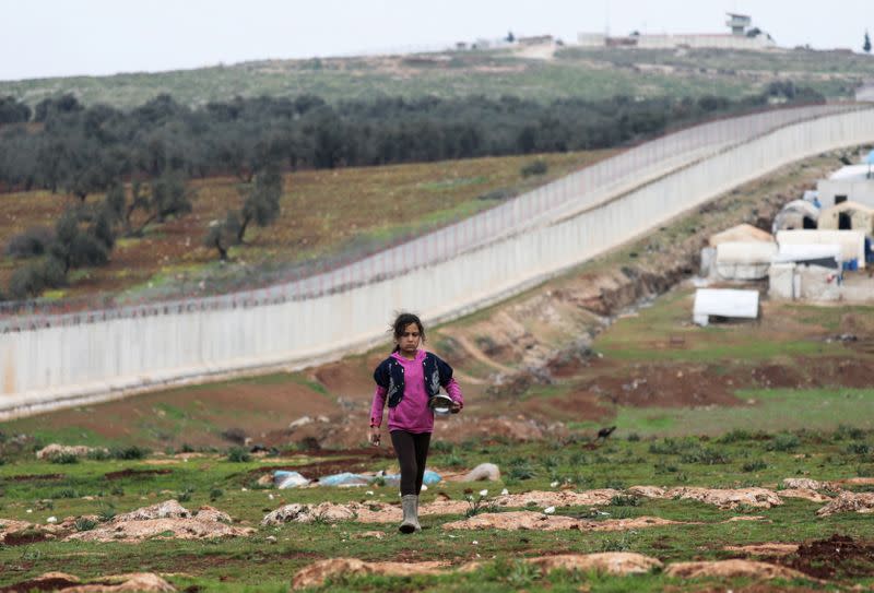 An internally displaced Syrian girl walks past the wall in Atmah IDP camp, located near the border with Turkey